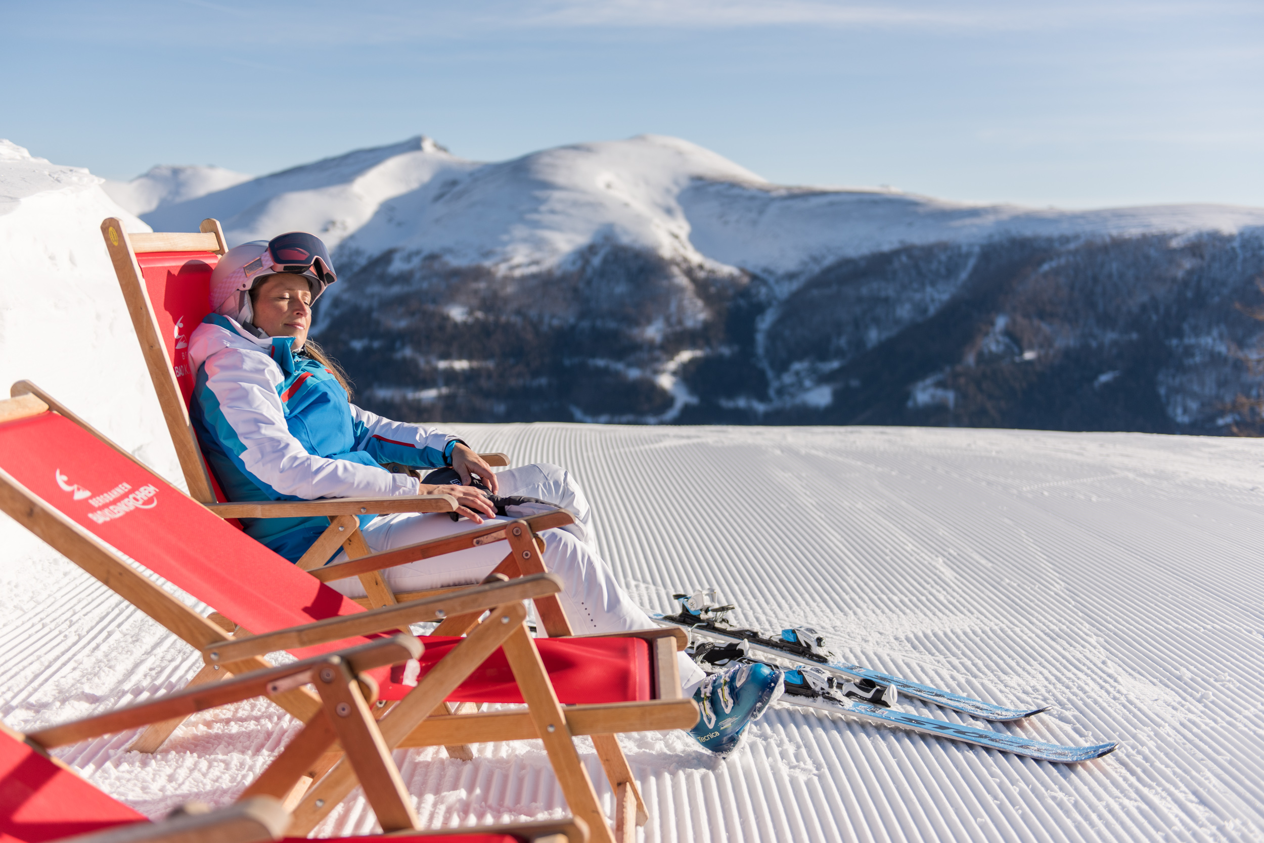 A woman taking a break from skiing and enjoying the sun in a deck chair.