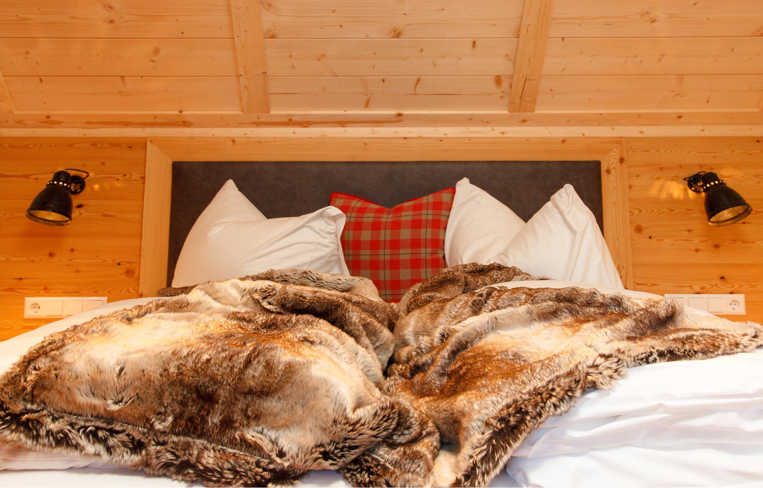 Ein Doppelbett befindet sich in einem Chalet-Zimmer aus Holz