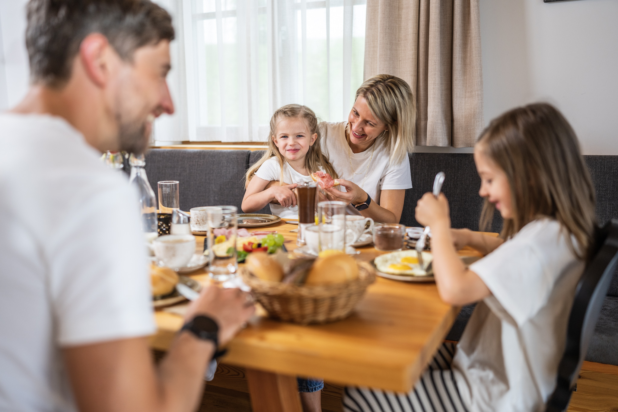 Eine vierköpfige Familie die am voll gefühlten Frühstückstisch sitzt und Frühstückt.